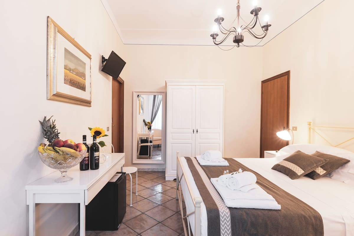 A hotel room with a bed, a desk with a fruit bowl, a mirror, and a wardrobe.