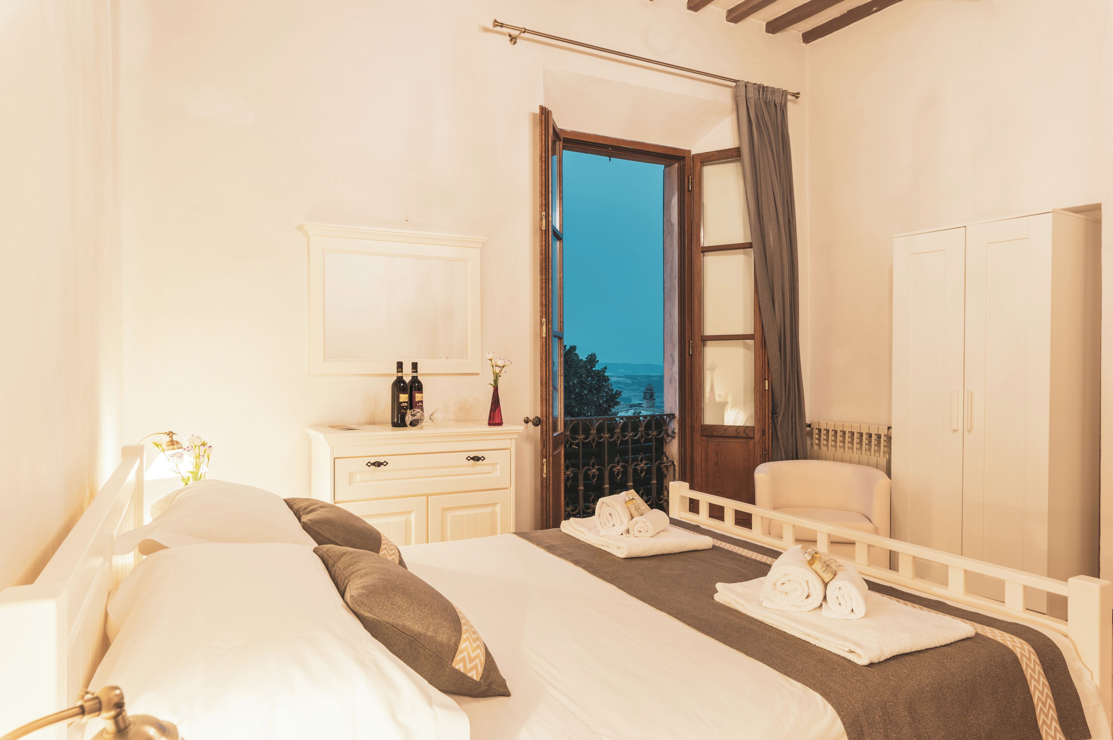 Habitación de hotel con cama, mesita de noche, espejo, armario y vista al exterior.