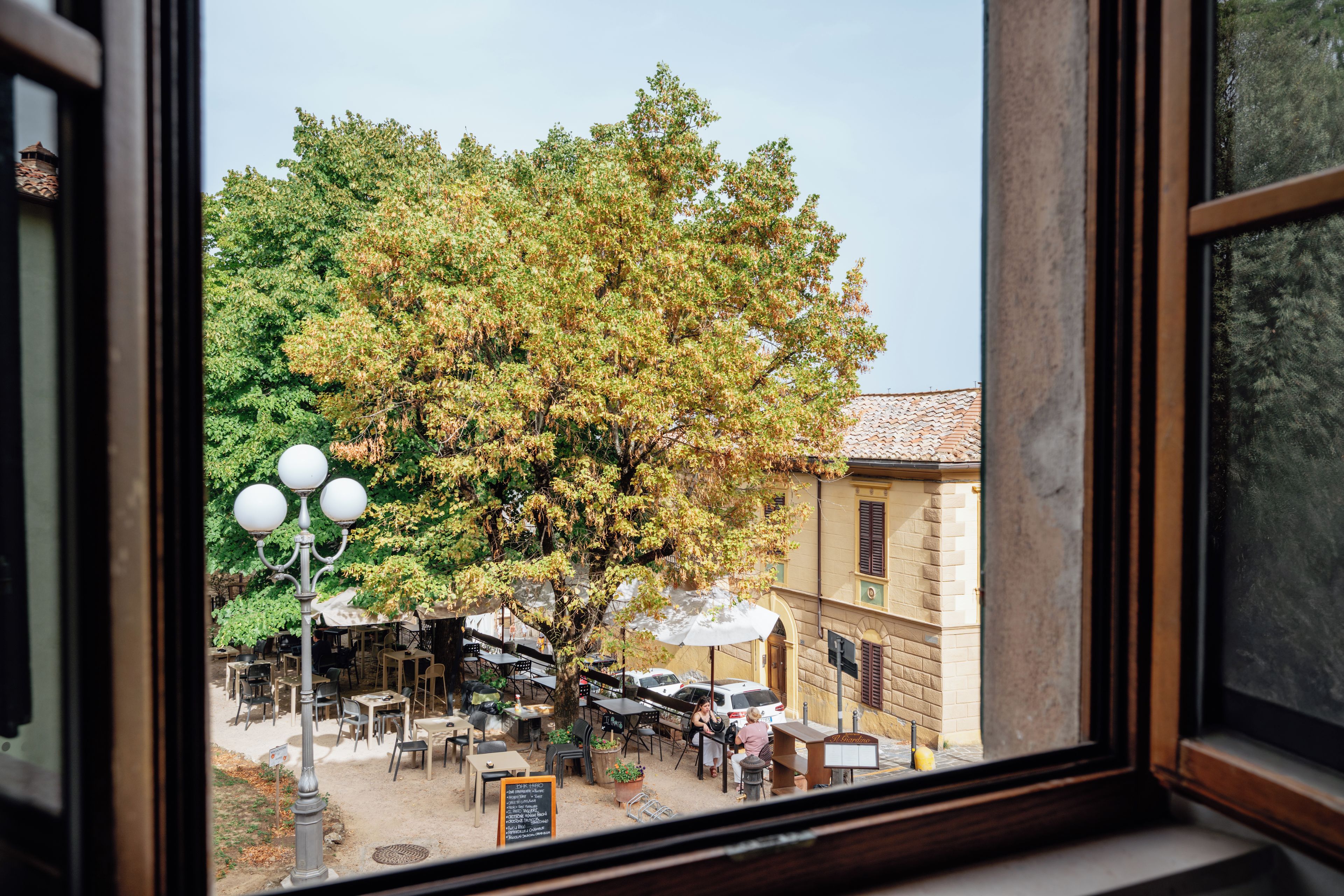 Vista di una zona con posti a sedere all'aperto, tavoli, sedie, un lampione e un albero.
