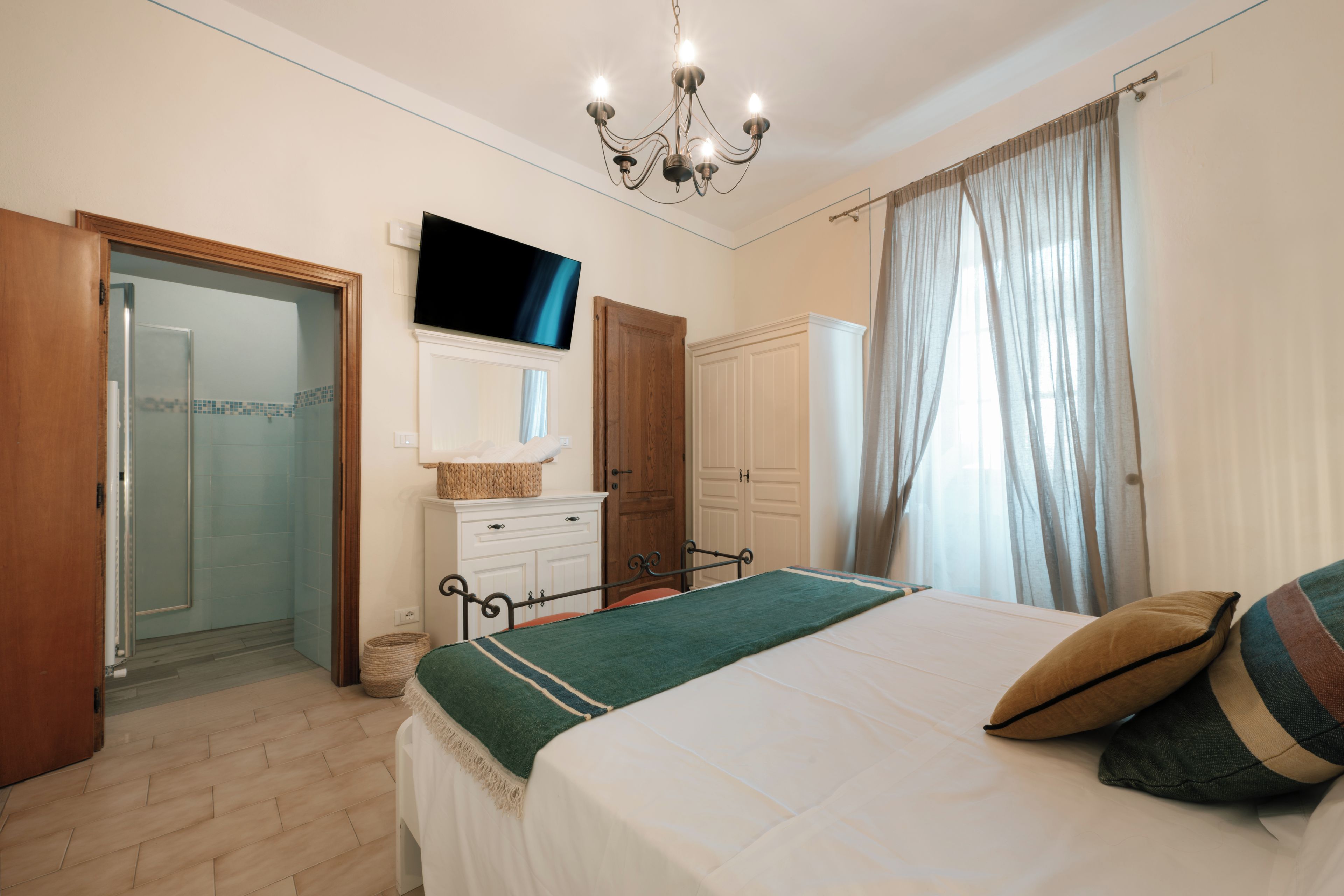 Une chambre à coucher comprenant un lit, un téléviseur fixé au mur, une armoire en bois et une salle de bain avec une porte en verre.