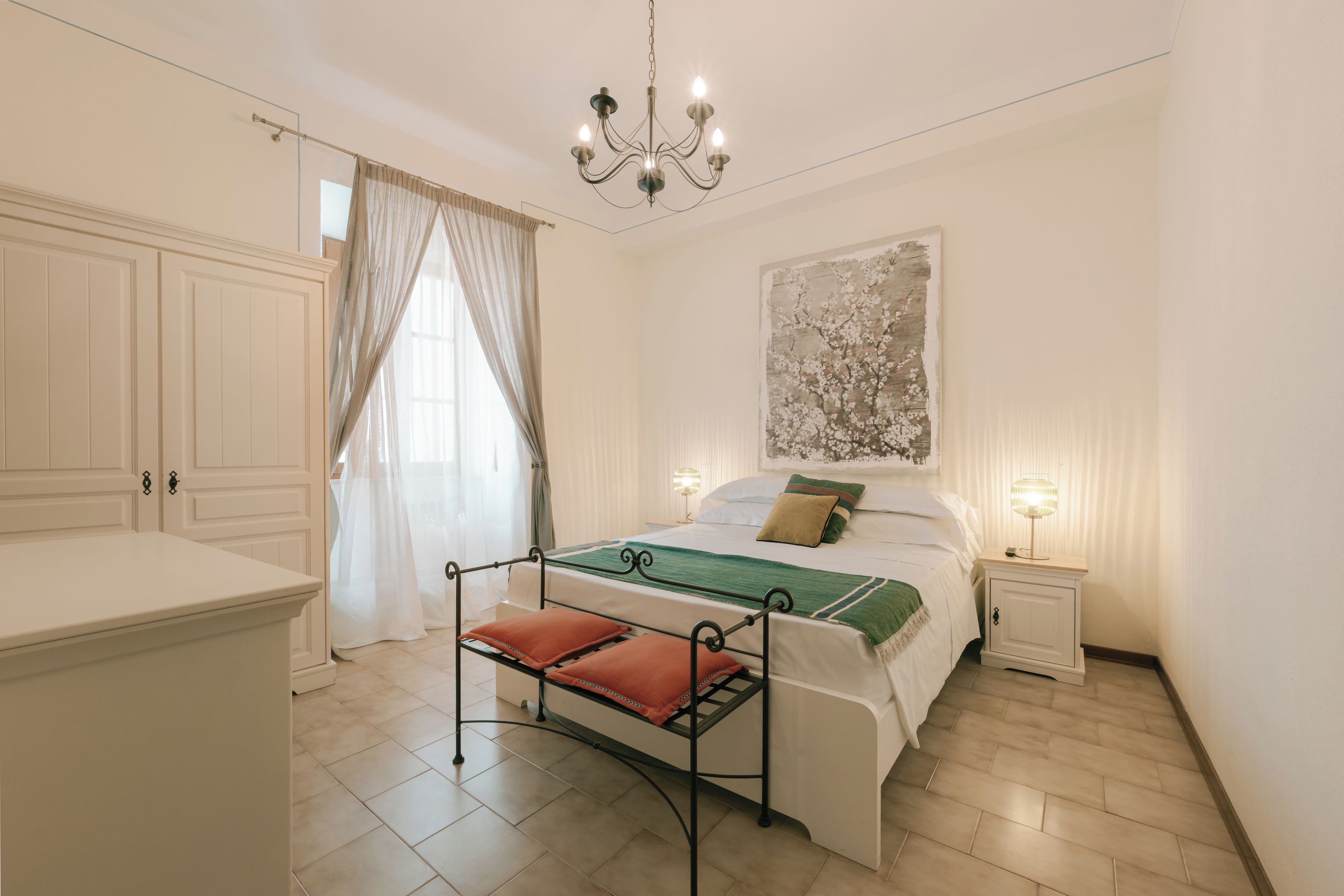 A bedroom with a bed, bedside tables, a chandelier, and a painting on the wall.