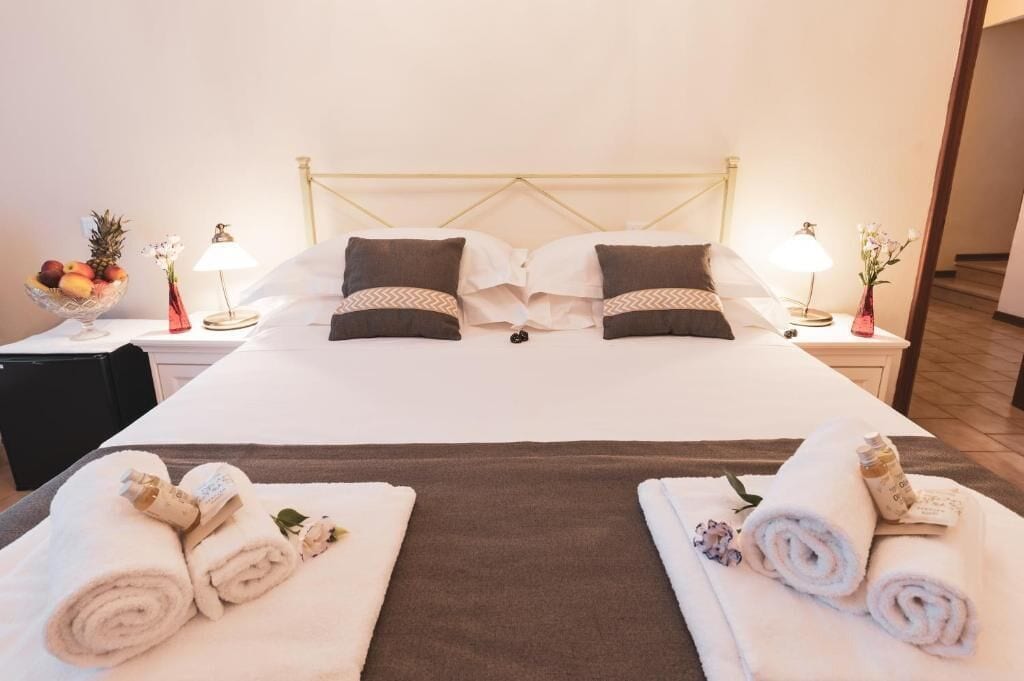 A hotel room with a bed, two bedside tables, a fruit bowl, and towels.