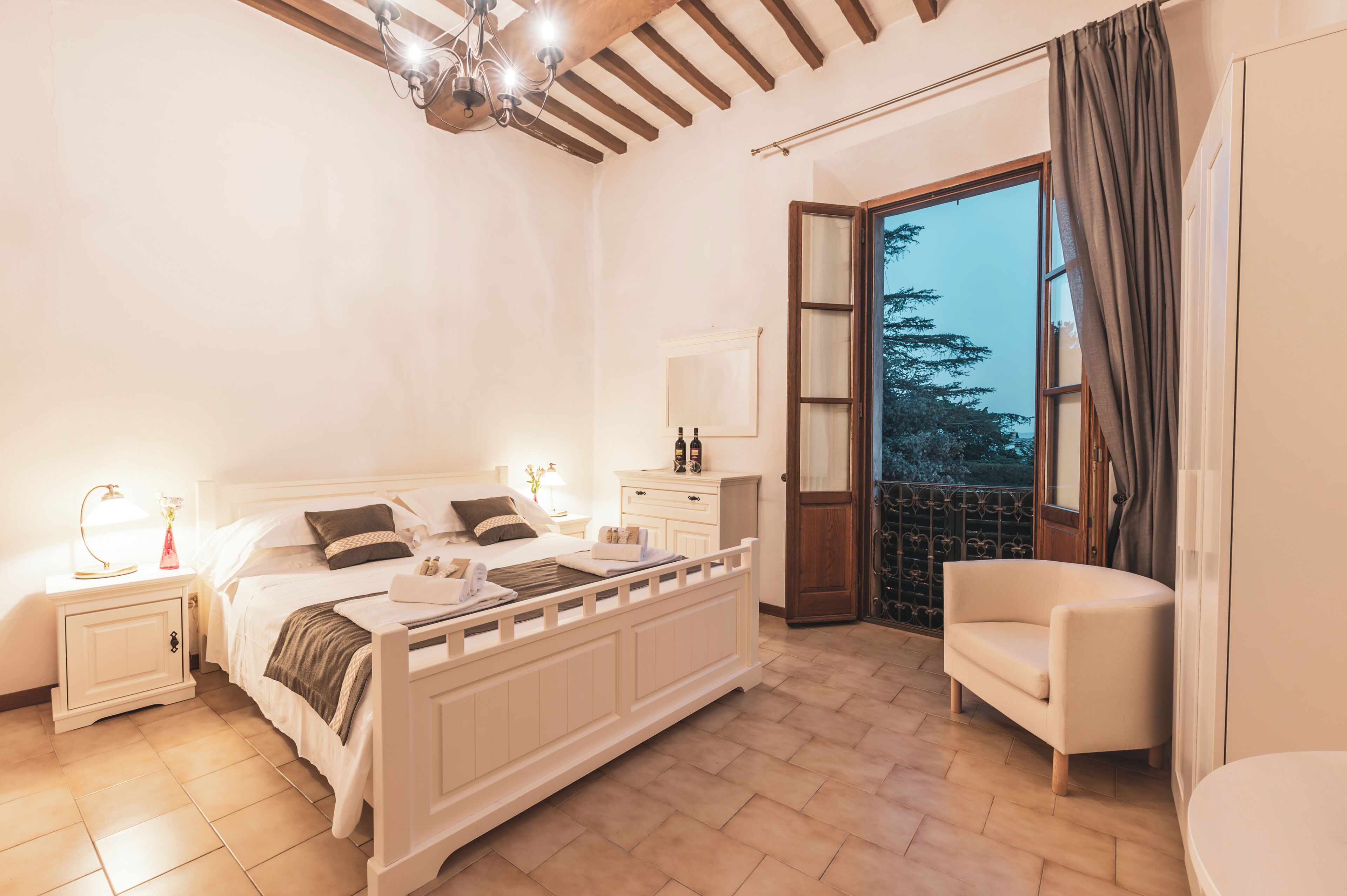 Una camera da letto con un letto, comodini, una sedia, una cassettiera e un balcone con vista.