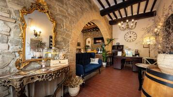 Interior rústico com paredes de pedra, um espelho grande e ornamentado, um sofá azul e uma mesa de centro de madeira.