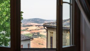 Blick aus einem Fenster auf eine ländliche Landschaft mit Feldern und sanften Hügeln in der Ferne.