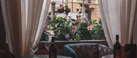 A restaurant with a view through sheer curtains, featuring round tables and patterned cushions.