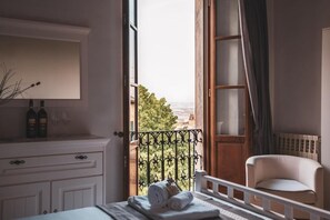 Una stanza con un letto, una sedia, vista attraverso una finestra aperta e un comò bianco con bottiglie e bicchieri.
