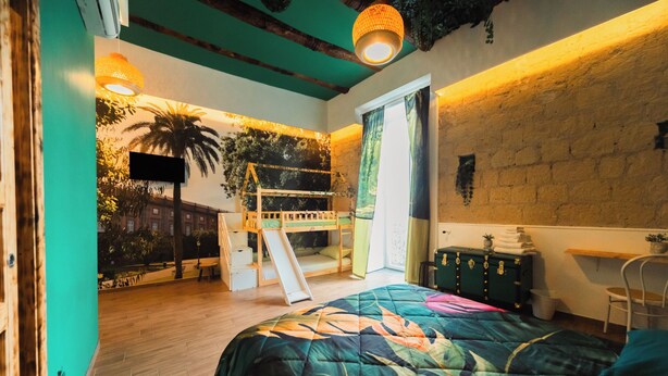 Una habitación con literas, un escritorio, una silla, un ventanal con cortinas, un televisor montado en la pared y una lámpara en el techo.