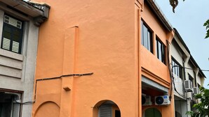 A building with a distinctive orange facade, a closed shutter door, and a visible air conditioning unit. - Pine Armenian (George Town)