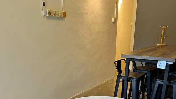 A room with a round white table surrounded by four stools, a wooden table with chairs, and a wall-mounted electrical outlet. - Pine Armenian (George Town)