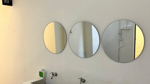 A white bathroom with three round mirrors mounted on the wall above a rectangular sink with two faucets. - Pine Armenian (George Town)