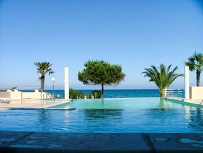 En swimmingpool med utsikt över havet, omgiven av palmer och en klar himmel.