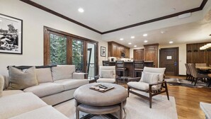 A spacious living room with a large sectional sofa, a round ottoman, and a dining area with a wooden table and chairs. - The Charter at Beaver Creek C110 (Beaver Creek)
