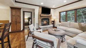 A spacious living room with a stone fireplace, comfortable seating, and a large window offering a view of trees. - The Charter at Beaver Creek C110 (Beaver Creek)