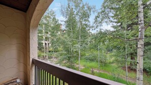 Un balcon donnant sur une zone boisée, avec un bâtiment visible au loin.