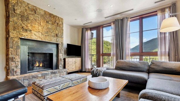 A living room with a stone fireplace, a sofa, a coffee table, and a television. - Solaris 6G East - 4 Bedroom (Vail)