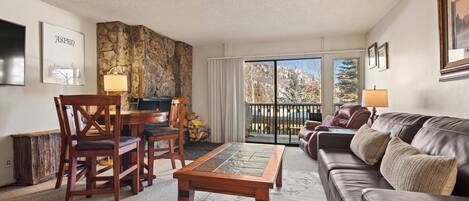 A living room with a stone wall, a wooden coffee table, a leather sofa, and a dining area with chairs and a table.