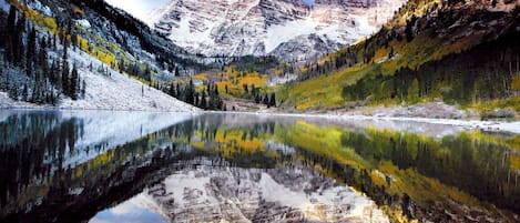 A mountain lake with reflections of the surrounding mountains and trees.