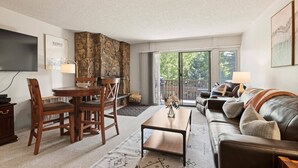A living room with a dining area, a sofa, a TV, and a stone accent wall. - Lichenhearth 23 (Snowmass Village)