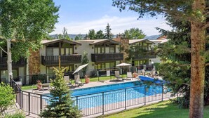 A hotel with multiple-story buildings, outdoor swimming pool, and lounge area with chairs and umbrellas. - Lichenhearth 23 (Snowmass Village)