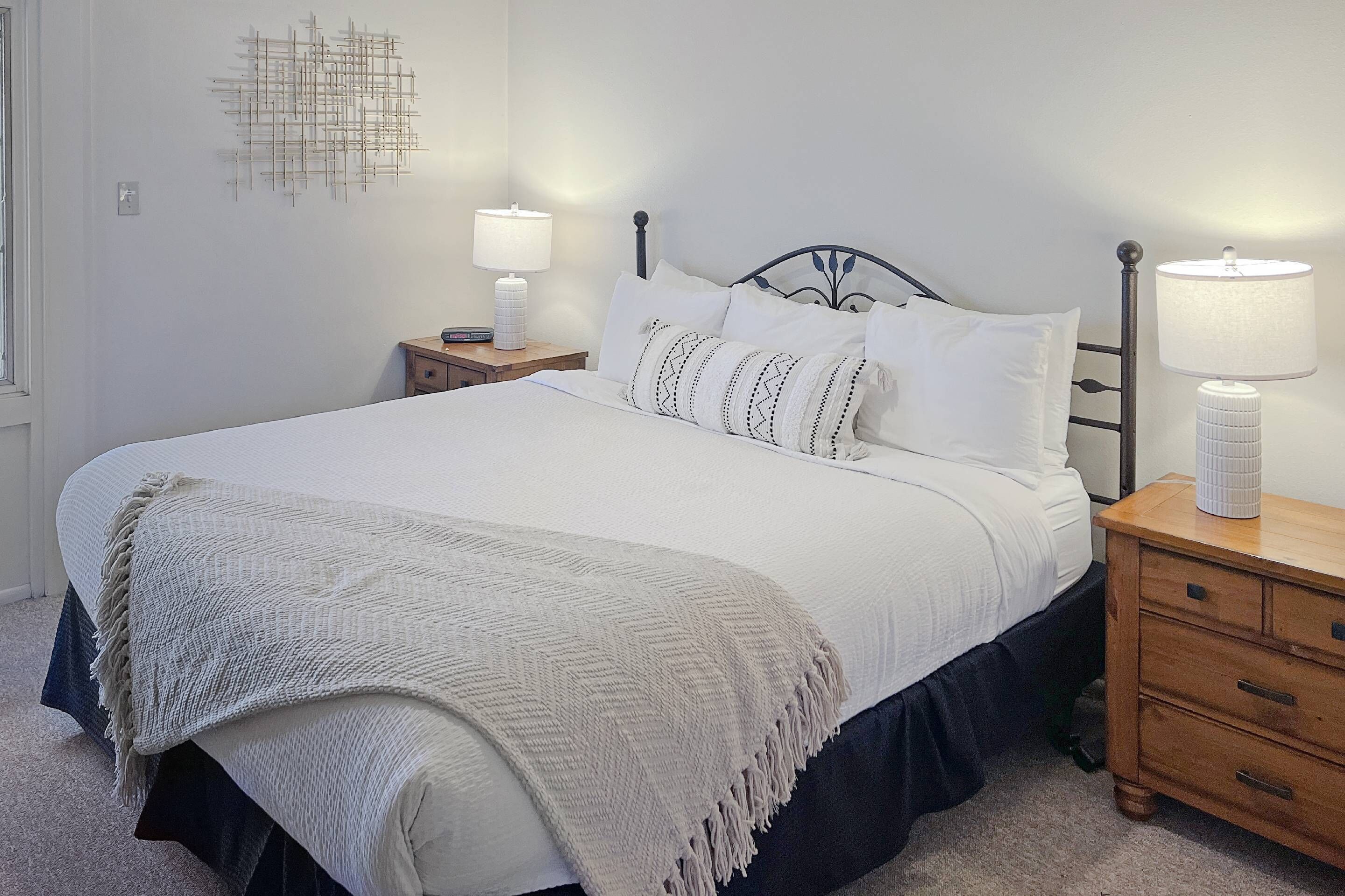A neatly made bed with white bedding and a decorative throw blanket. There are two bedside tables with lamps, and a wall-mounted light fixture.