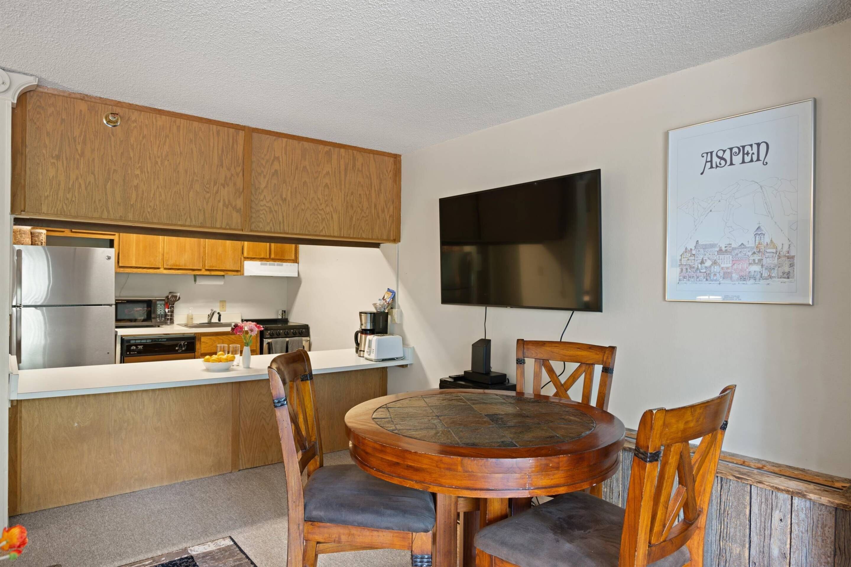 A compact kitchen with wooden cabinets, a built-in microwave, and a dining area with a round table and four chairs.