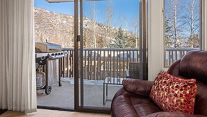 A room with a sliding glass door leading to a balcony with a barbecue grill and a view of snow-covered hills. - Lichenhearth 23 (Snowmass Village)