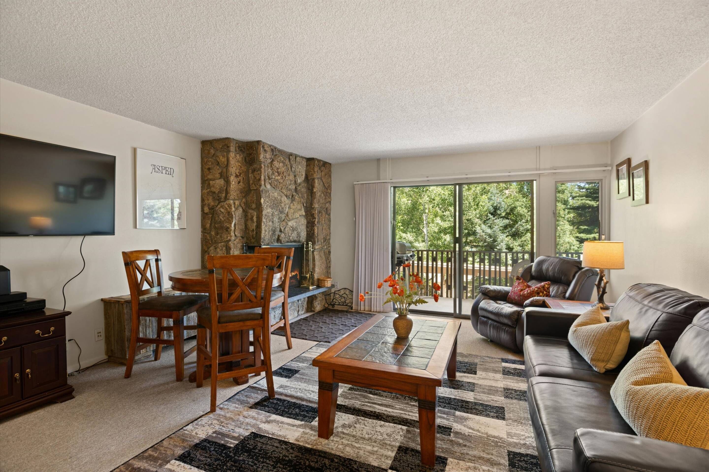 A living room with a stone accent wall, a fireplace, a sofa, a coffee table, and a dining area with chairs and a TV.