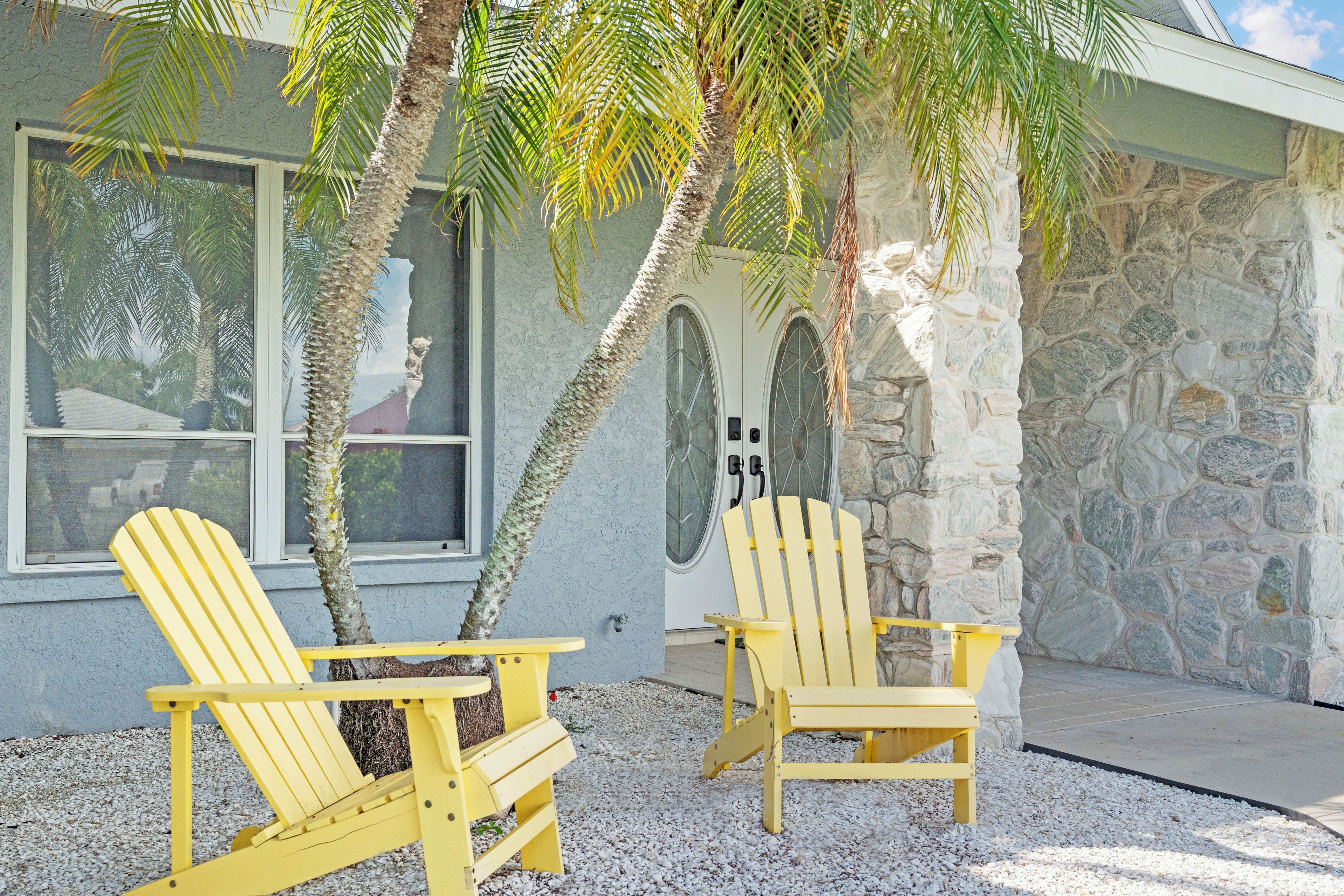 Two yellow Adirondack chairs outside a building with a stone facade and a window.