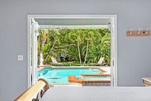 A room with a view of a swimming pool, a bed, and a window.