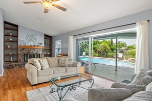 A living room with a sofa, a glass coffee table, a fireplace, and a view of a swimming pool.