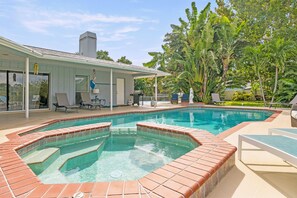 A swimming pool with a hot tub, surrounded by a covered patio with chairs and a table.
