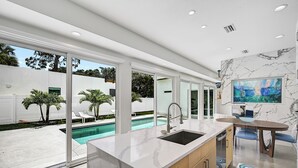 A modern kitchen with a large island, a built-in sink, and a view of a swimming pool. - Luxury Home, Pool, Mins to Top Beaches and Downtown Sarasota (Sarasota)