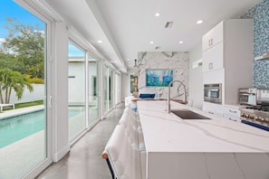 A modern kitchen with a large island, stainless steel appliances, and a view of a swimming pool.