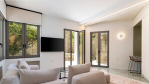 Un salon moderne avec un canapé beige, un téléviseur à écran plat fixé au mur et une porte vitrée donnant sur un espace extérieur.