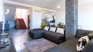A modern living room with a sectional sofa, a stone pillar, and a staircase leading to a kitchen area. - GuestReady - Spacious stay with sea views (Caniço)