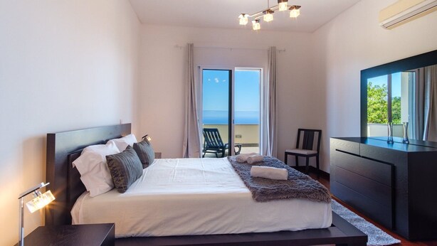 A modern bedroom with a large bed, a desk, and a view of the sea. - GuestReady - Spacious stay with sea views (Caniço)