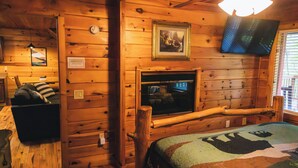 A cozy cabin interior with wooden walls, a bed with a quilt, a mounted television, and a wooden bench.