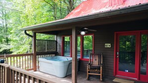 A wooden deck with a hot tub, a chair, and a red door.