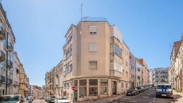Un immeuble à plusieurs étages, avec un espace commercial au rez-de-chaussée, des voitures garées et un ciel bleu dégagé.