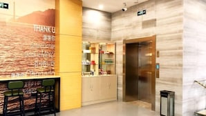 Zona de recepción de un hotel con pared de mármol, mostrador de recepción y una vitrina de vidrio.