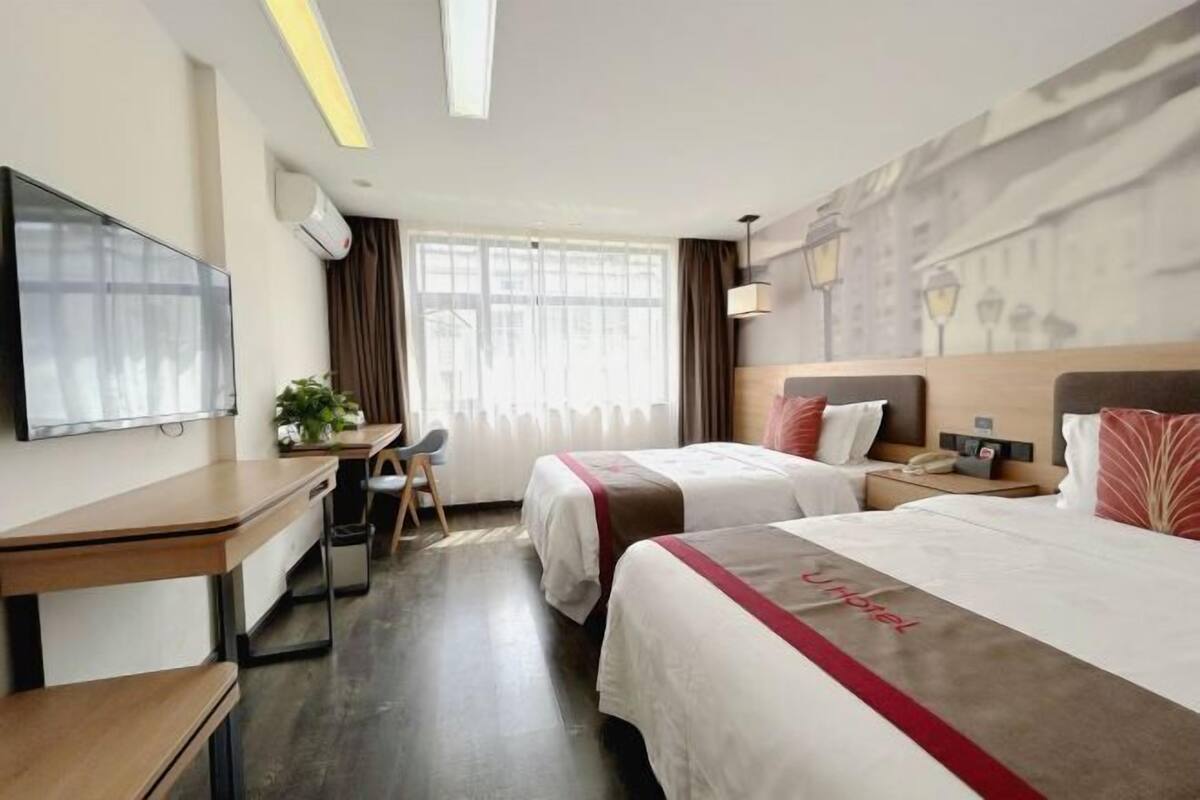 A hotel room with two beds, a desk, a chair, a TV, and a window with curtains.