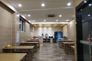 A dining area with multiple tables and chairs, a counter with a blue door, and a tiled floor. - Shankee Chain Hotel (Yancheng Municipal Government Jinying Julonghu Store) (Yancheng)