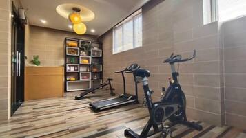 Een sportschool met trainingsapparatuur, een houten vloer, een wandplank met spullen en een plafondlamp.