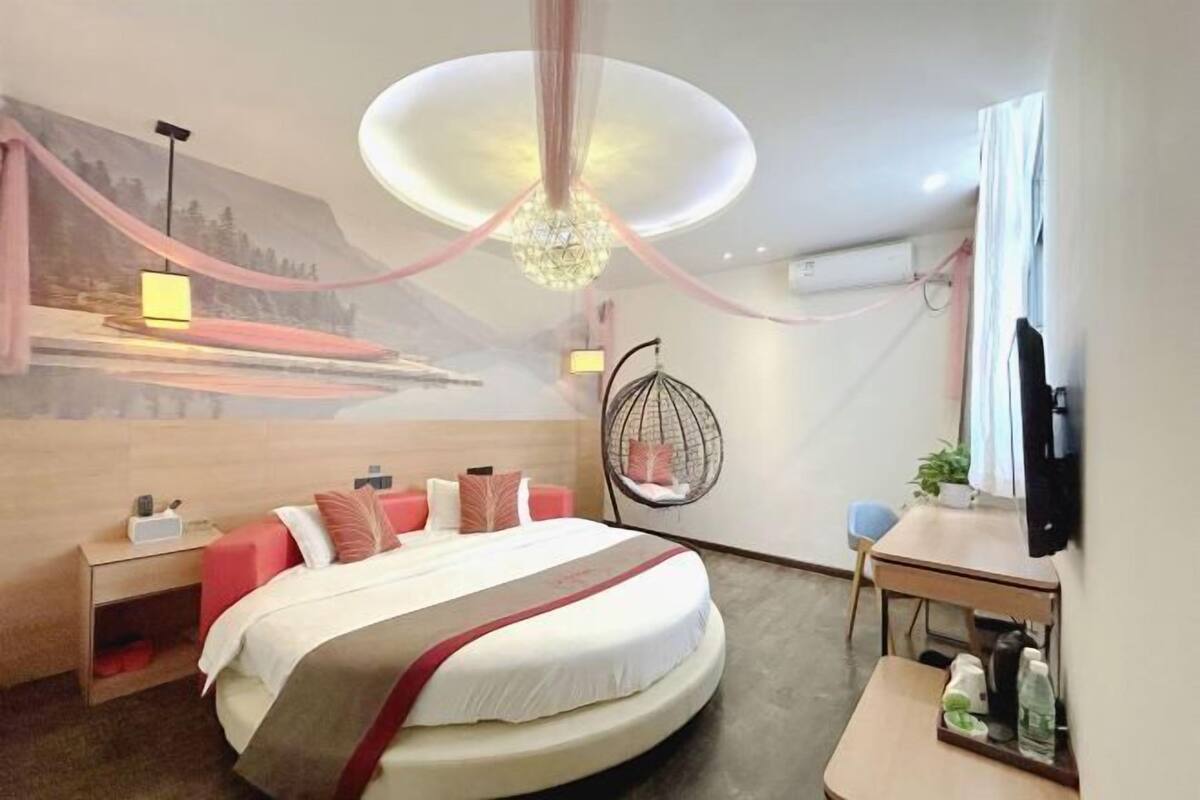 A hotel room with a round bed, a desk, a chair, a hanging chair, and a TV.