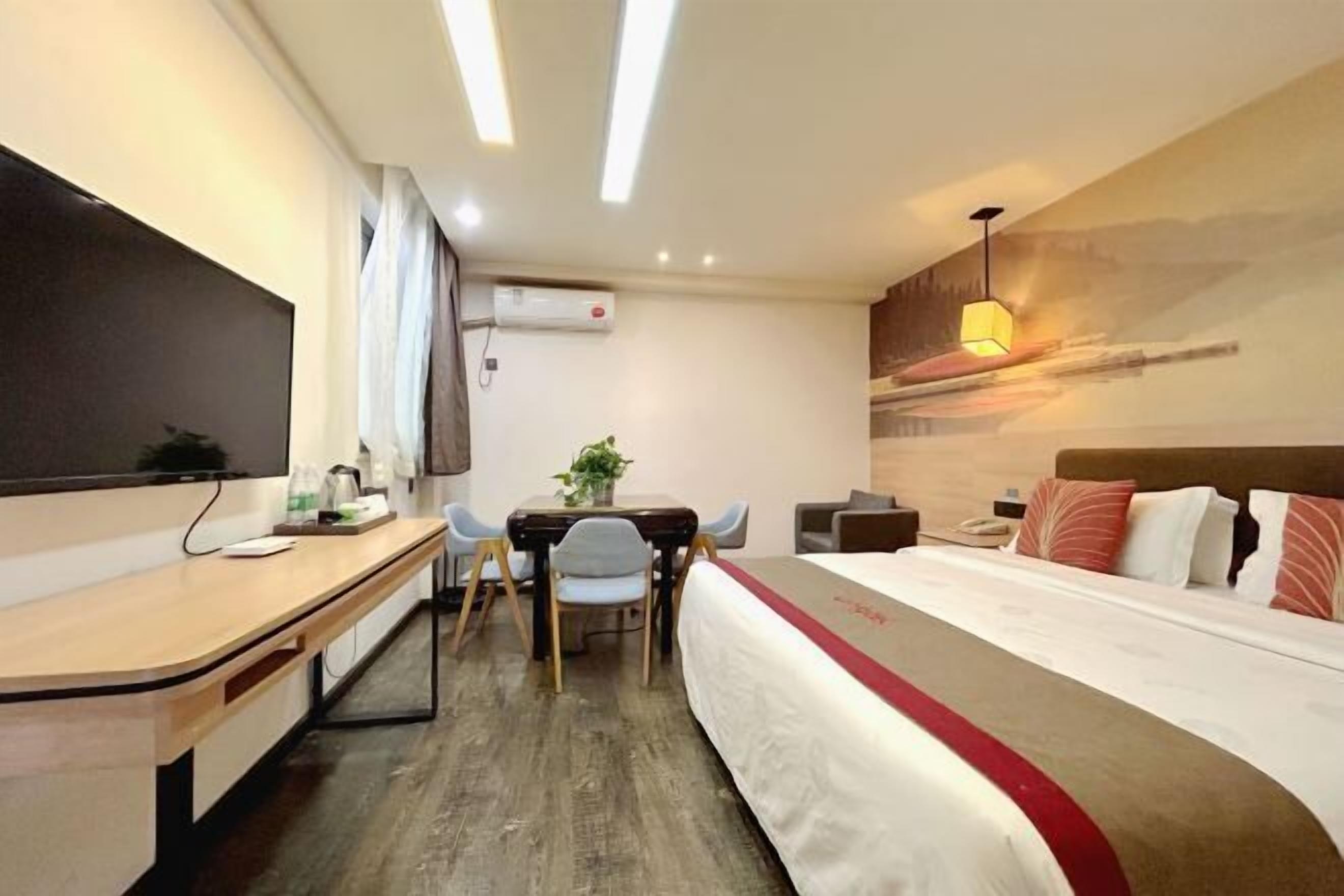 Habitación de hotel con cama, escritorio, silla, pequeña mesa con planta y aire acondicionado instalado en la pared.