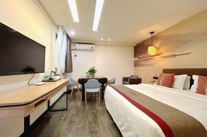 Habitación de hotel con cama, escritorio, silla, pequeña mesa con planta y aire acondicionado instalado en la pared.