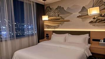 Habitación de hotel con cama, mesita de noche, lámpara, vista nocturna de la ciudad y un mural en la pared.
