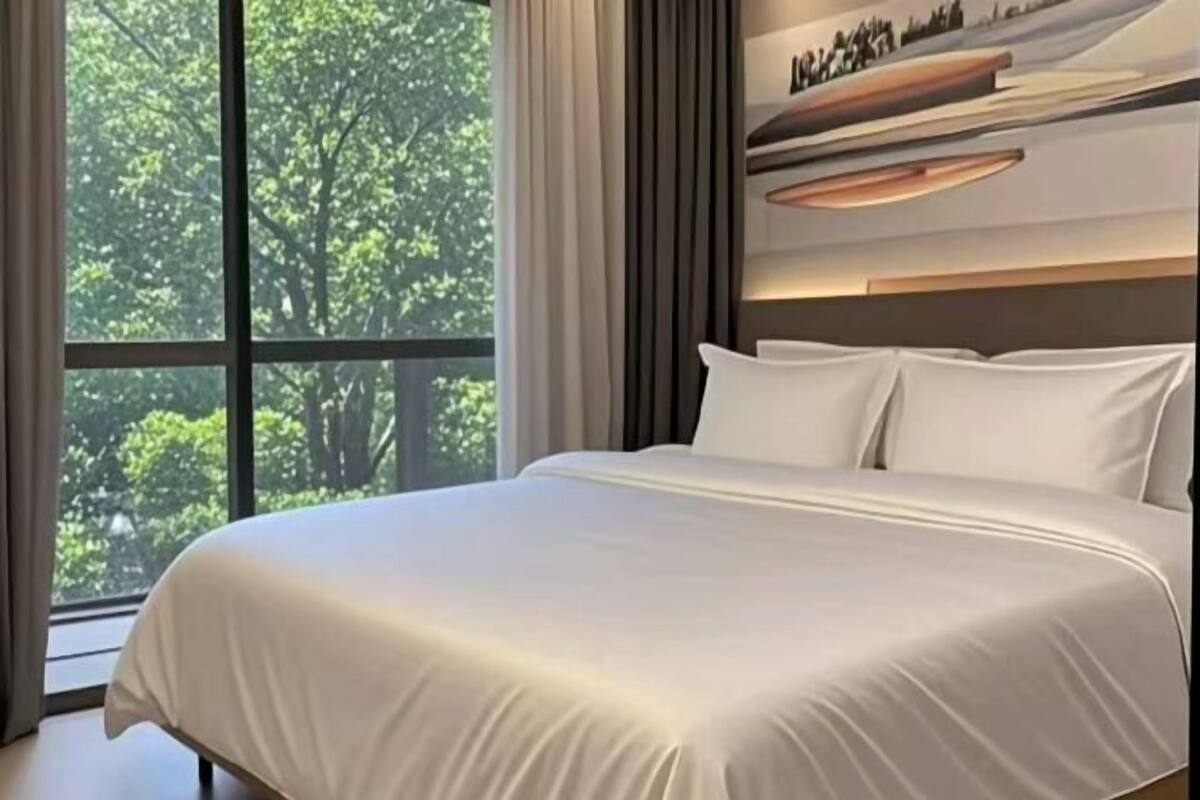 A modern bedroom with a large window, a bed with white linens, and a minimalist decor.