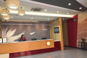 Balcão de recepção com recepcionista, parede com padrão de pena e parede com detalhes em vermelho.